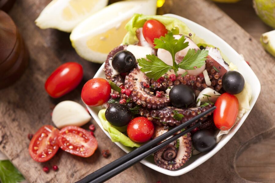 Colorful seafood salad with octopus, tomatoes, olives, garlic, parsley, and lemon accents.