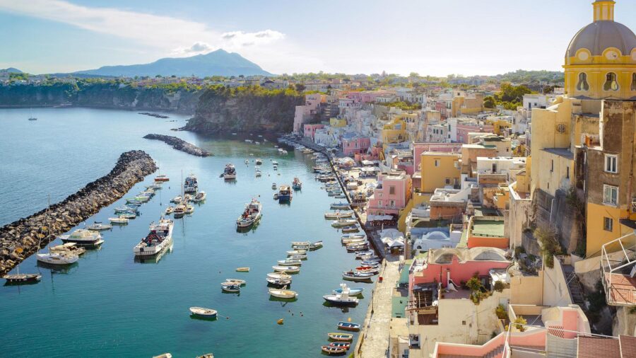 Procida harbor with pastel houses, breakwater, and moored boats.