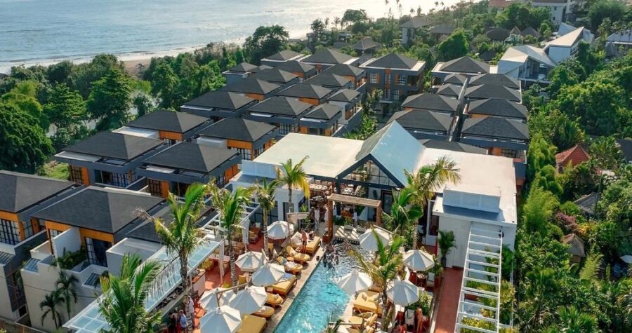 Aerial view of luxury beachfront resort with villas, infinity pool, palm trees, and ocean views.