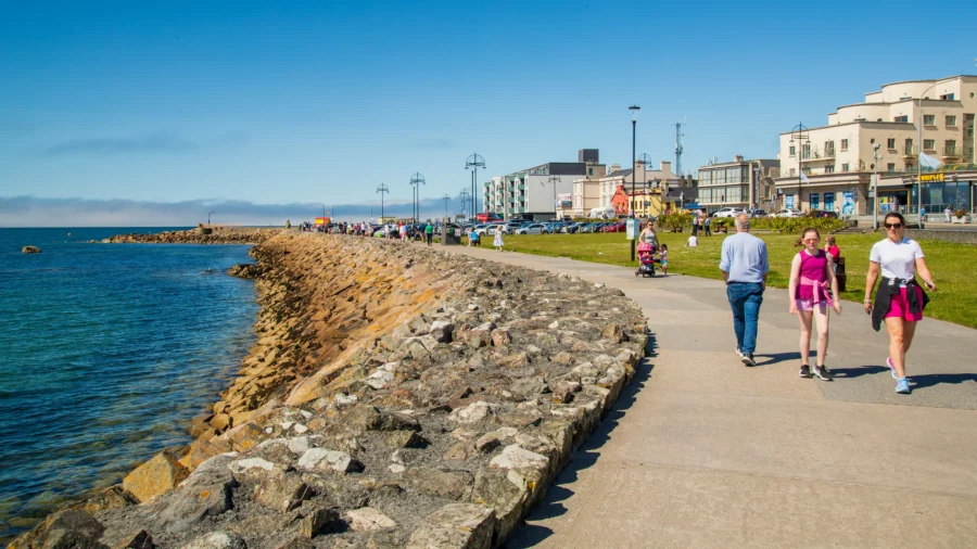 Salthill Promenade sunny seaside walkway with seawall, lamps, and people strolling.