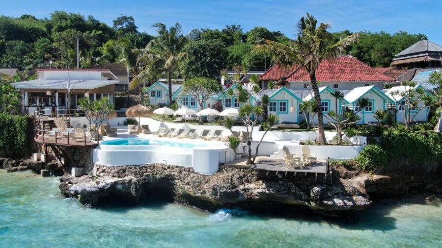 Tropical seaside resort with infinity pool, white bungalows, rocky coastline, and turquoise ocean views.