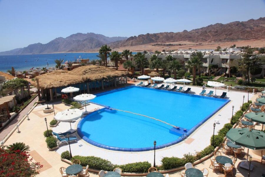 Red Sea resort pool with umbrellas, palm trees, beach, and desert mountains in Dahab, Egypt.