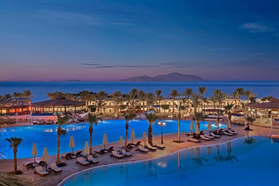 Luxury seaside resort with illuminated pools, palm trees, and ocean view at twilight in Sharm El Sheikh.