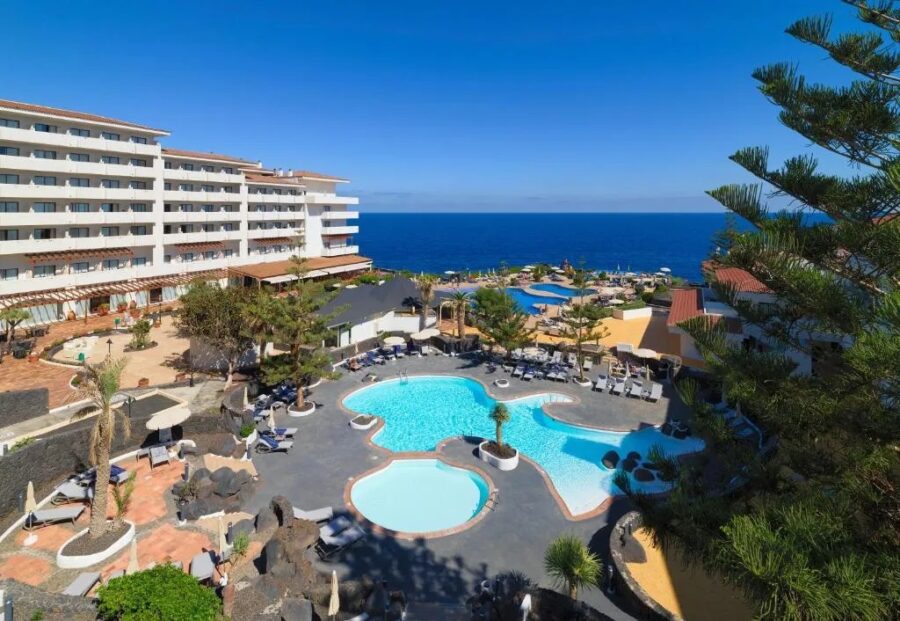 Luxury seaside resort in La Palma with ocean view, infinity pools, palm trees and sun loungers.