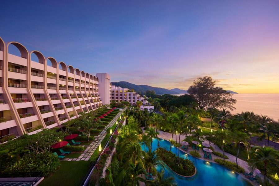 Luxury Penang beach resort at sunset with lagoon pool, palm trees, balconies and ocean views.