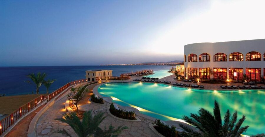 Luxury seaside resort at twilight with infinity-style pool, ocean views, and illuminated hotel building.