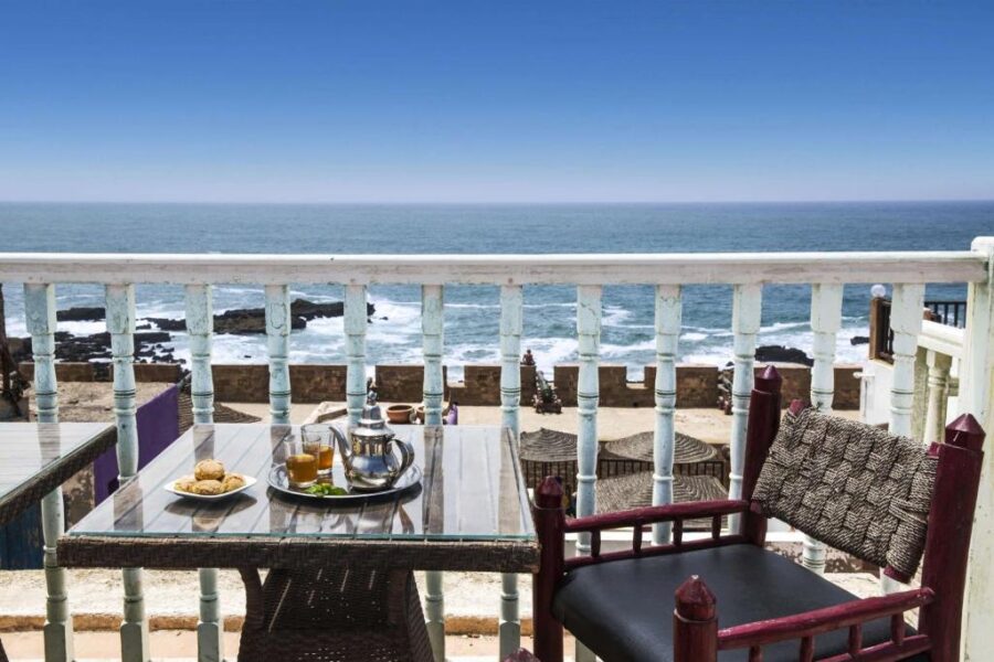 Oceanfront Moroccan balcony with mint tea, pastries, wicker chair and panoramic seaside view.