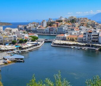 Mediterranean Crete coastal harbor with boats, cafes, and scenic architecture against a mountainous backdrop.