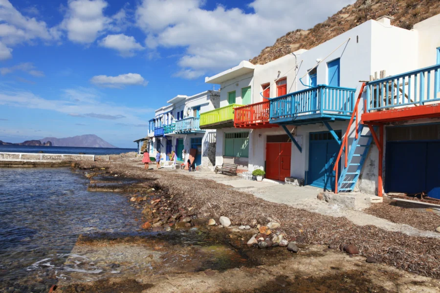 Milos seaside white houses with colorful shutters along rocky shore.
