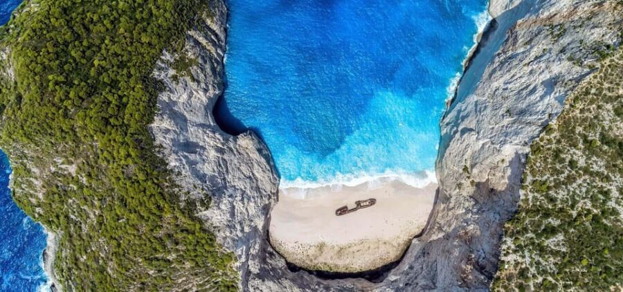 Aerial view of secluded cove with cliffs, azure waters, sandy beach, and shipwreck.