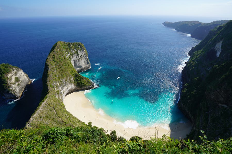 Clifftop view of secluded tropical beach cove with turquoise water, dramatic limestone cliffs, and boat.