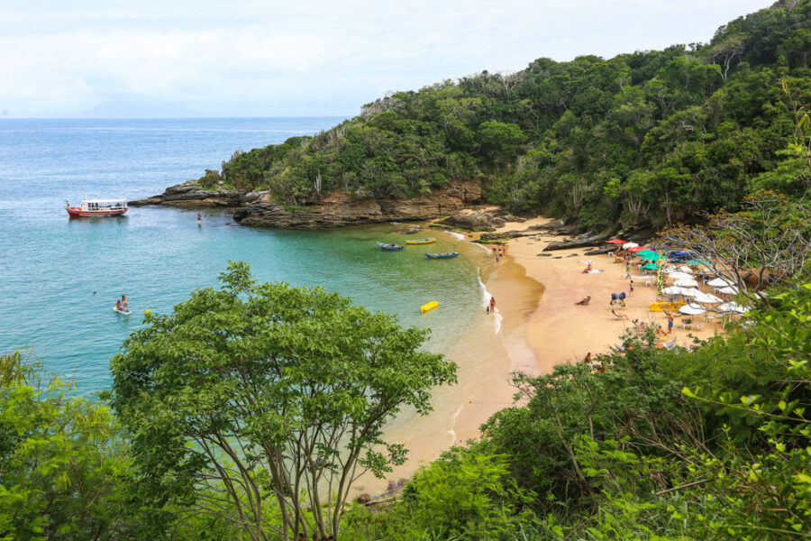 Secluded João Fernandinho Beach cove in Brazil with turquoise water, golden sand and umbrellas.