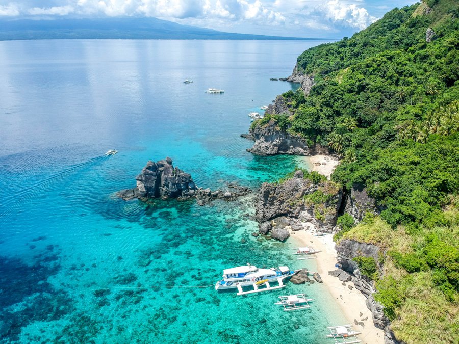 Apo Island, Philippines: secluded white-sand bay with turquoise water, forested cliffs, and boats.