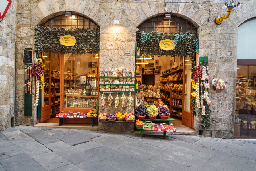 Charming local shop in Siena, Italy, featuring fruits, vegetables, cheese, and other regional products on a narrow street