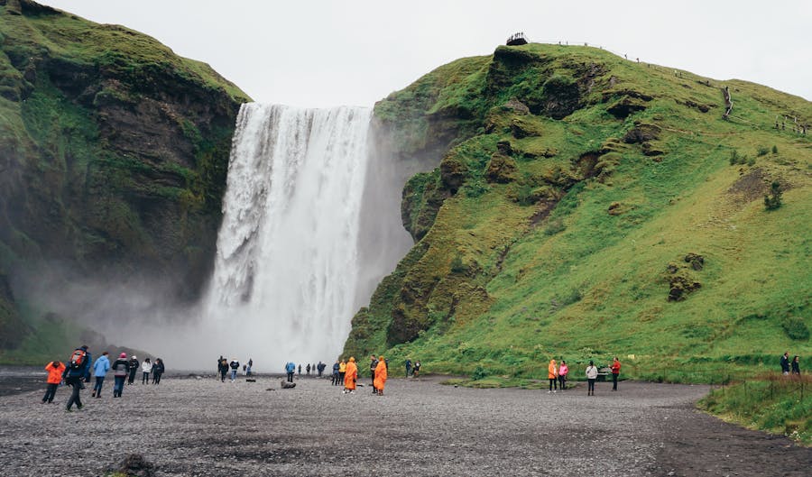 Seljalandsfoss waterfall in Iceland; lush greenery, mist, visitors in raincoats capture the beauty.