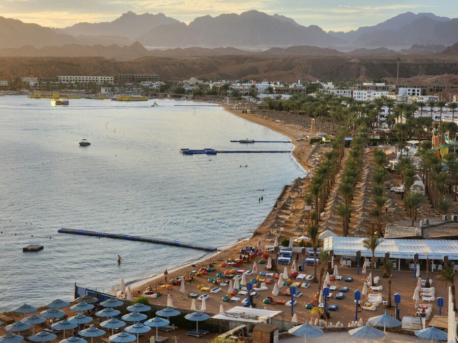 Luxury Red Sea resort beach with umbrellas, palm trees, calm bay waters and desert mountains.