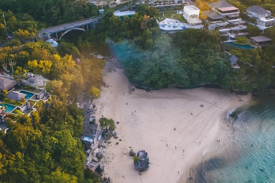 Aerial view of Kuta serene beach, lush greenery, resorts, and bridge at sunset.