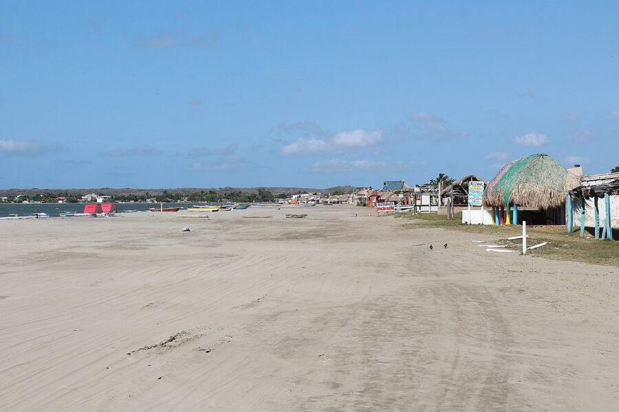 Tranquil beach with golden sand, fishing boats, blue sky, beach huts, and wildlife.