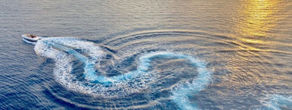 Golden sunset over ocean with boat, creating spiral waves. Tranquil and adventurous mood.