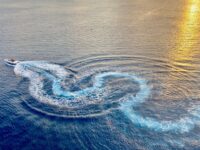Golden sunset over ocean with boat, creating spiral waves. Tranquil and adventurous mood.