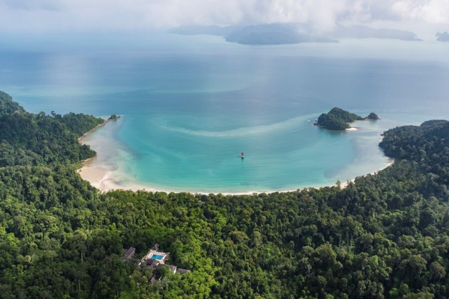 Aerial view of Teluk Datai tropical bay with beach, jungle, boat, and luxury resort.