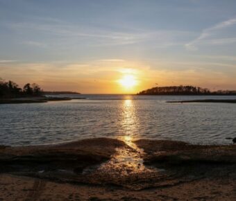 Cape Cod sunset over calm coastal landscape with island, reflecting golden hues on water.