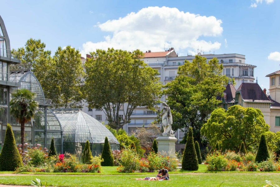 Tranquil park with lush greenery, vibrant flowers, couple relaxing, and glass conservatories.