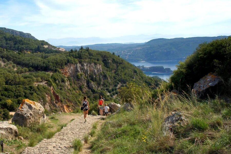 Hiking trail in lush landscape with hills, greenery, and hikers enjoying nature.