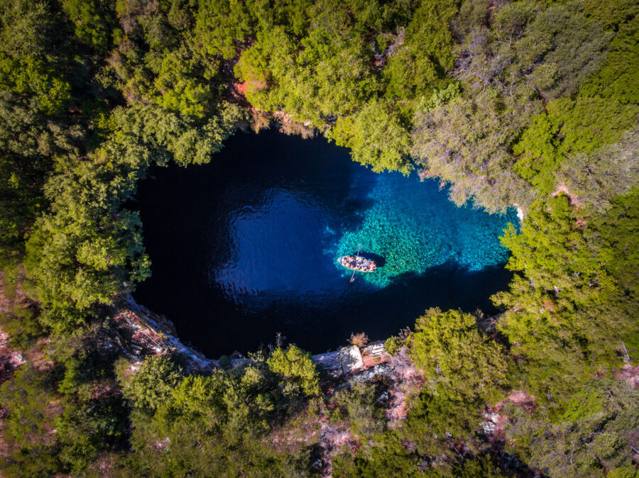 Serene lake surrounded by lush greenery and drifting boat in Melissani Cave.