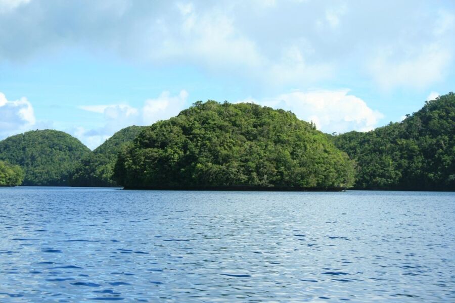 Serene landscape with lush green hills, calm waters, vibrant sky, and drifting clouds.