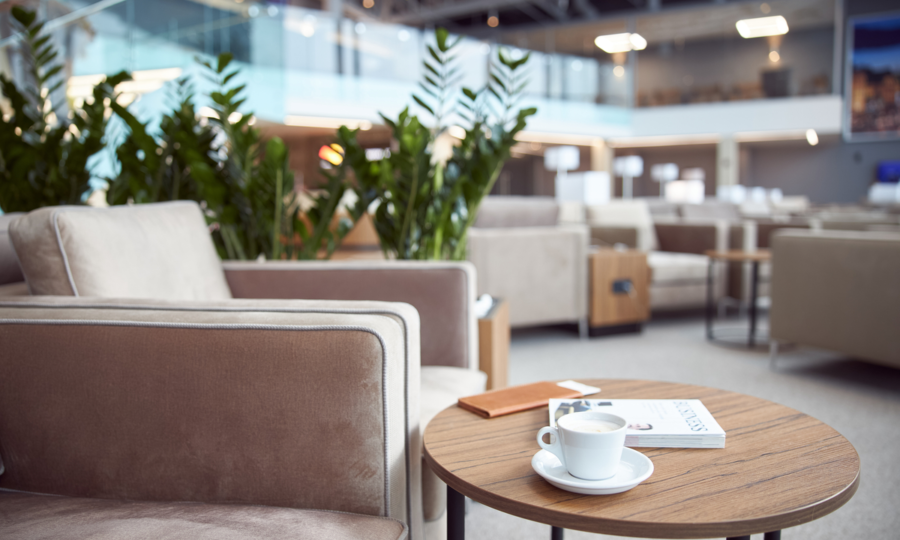 Modern lounge with beige armchair, wooden table, coffee, greenery, soft lighting, and open layout.
