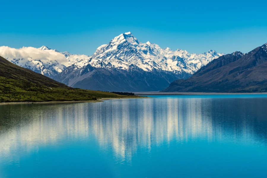 Turquoise alpine lake with snow-capped mountain reflection, clear blue sky and dramatic New Zealand landscape.