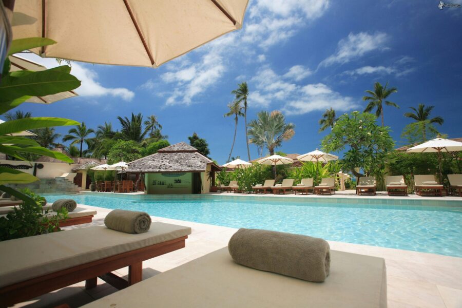 Tropical resort pool area with lush greenery, lounge chairs, parasols, and a relaxing atmosphere.