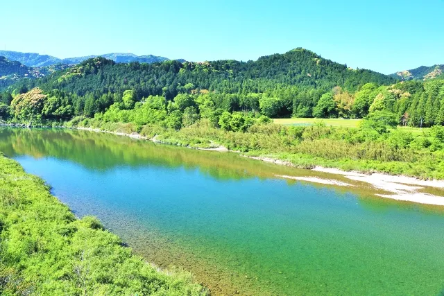 Miyagawa River flowing through clear turquoise water, lush green forest, and rolling hillside landscape.