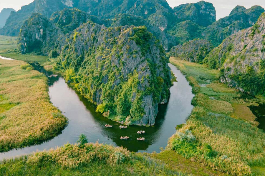 Boats on winding river in Van Long wetland surrounded by lush karst mountains and rice fields.