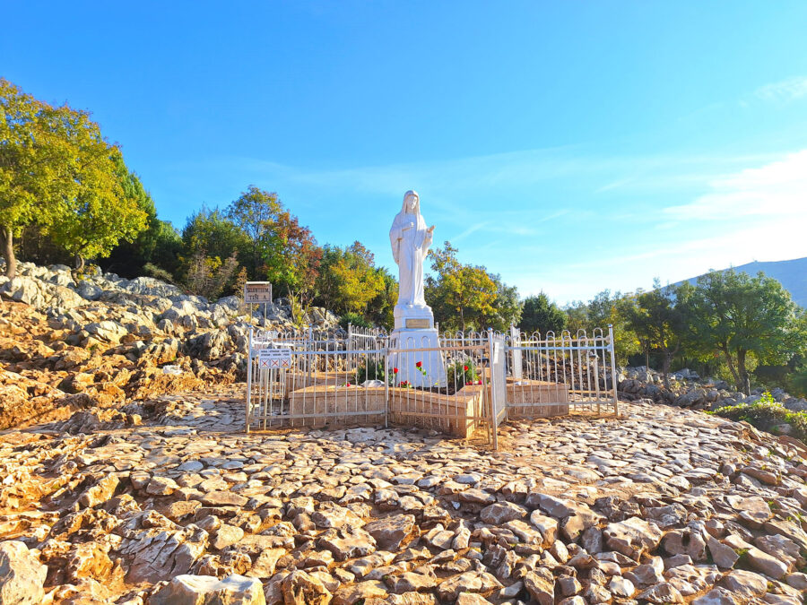 Statue in peaceful natural setting, surrounded by flowers and rocky terrain in Bosnia and Herzegovina.
