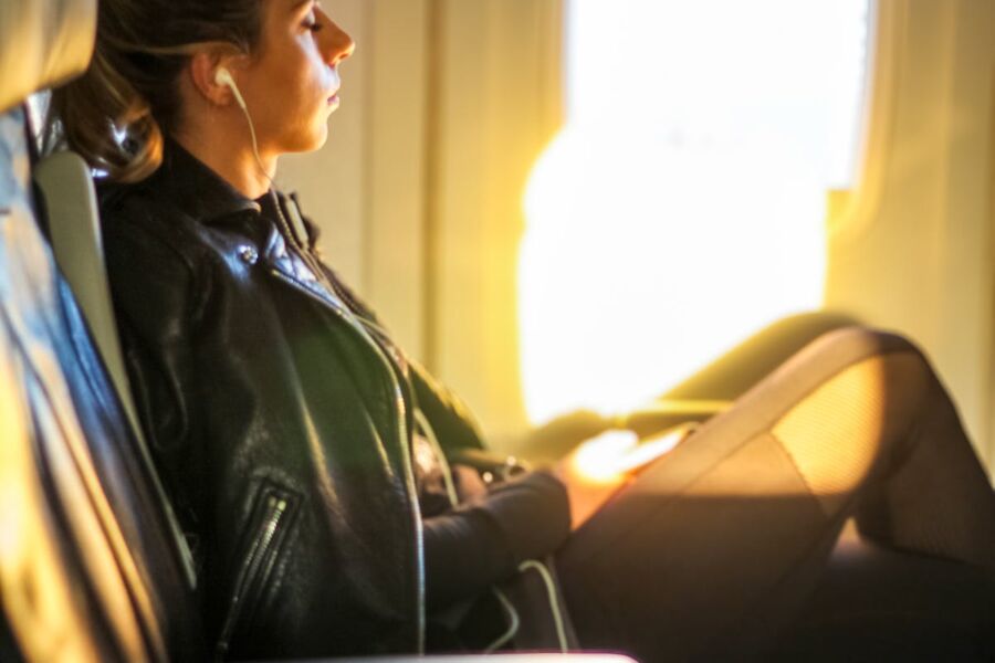 Young woman in leather jacket, contemplating on airplane, using earplugs 