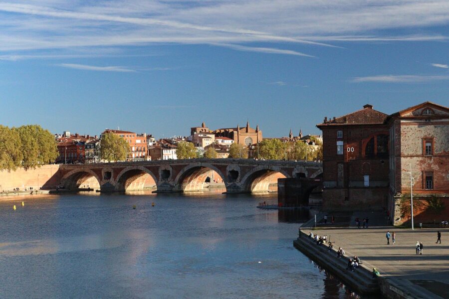 Historic bridge over river, arch architecture, green trees, urban backdrop, serene beauty.
