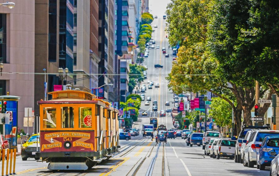 San Francisco cable car on a hilly street with urban architecture and vehicles.