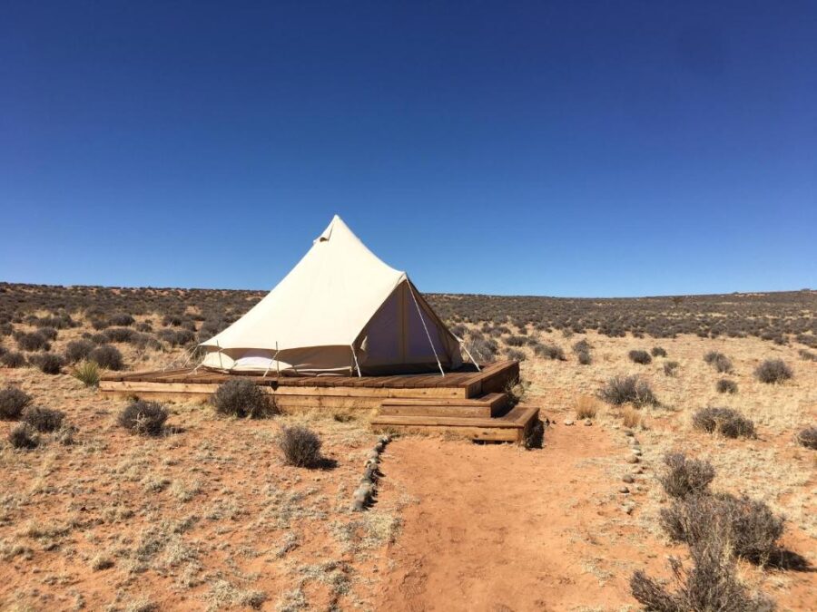 Desert scene featuring a tent on a wooden platform at Shash Dine EcoRetreat, Arizona, with a clear blue sky above.
