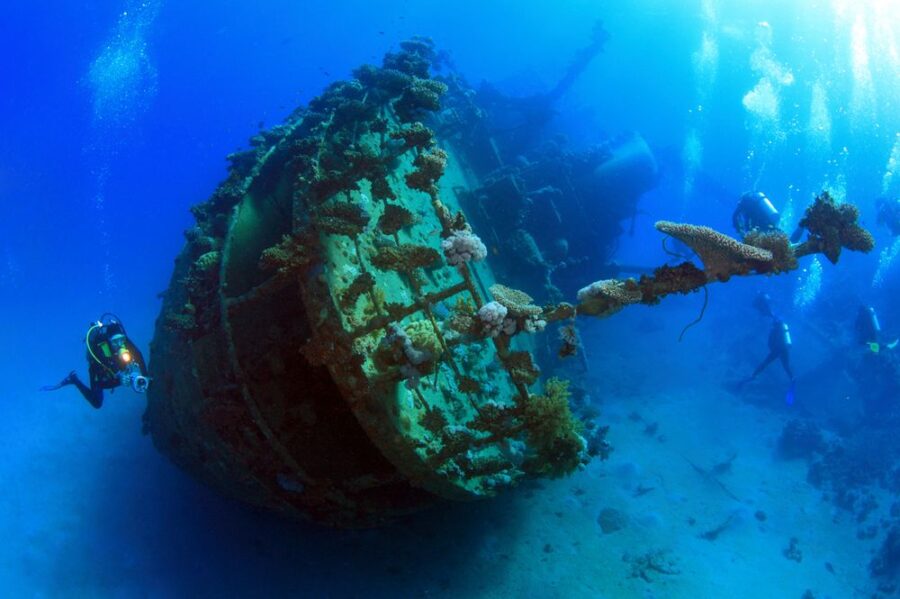 WWII shipwreck with scuba divers exploring underwater seafloor, corals, and marine growth.
