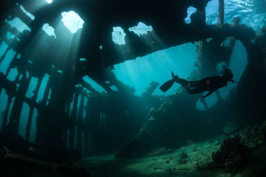 Free diver glides through a sunken shipwreck and underwater debris