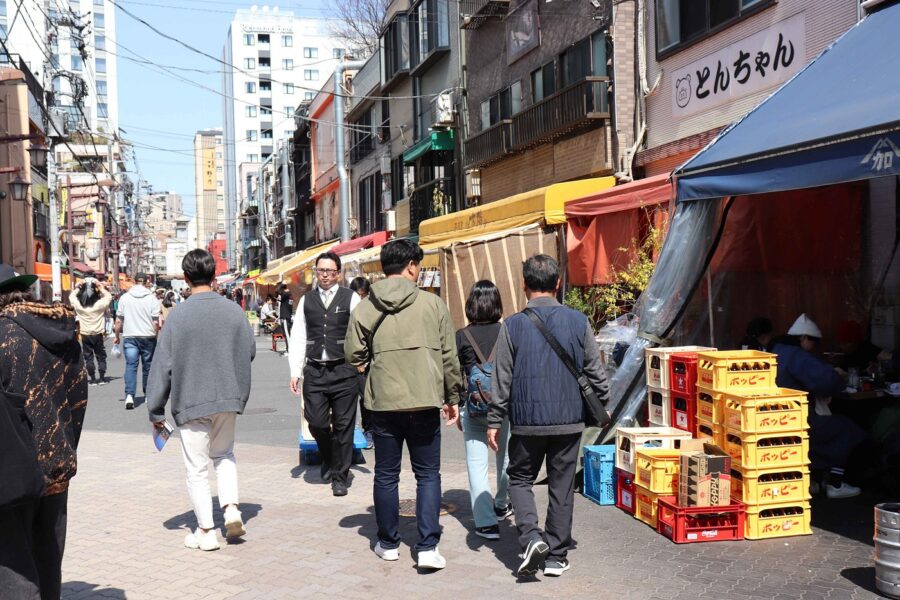 Japanese shopping street with pedestrians, izakaya stalls, and outdoor dining.