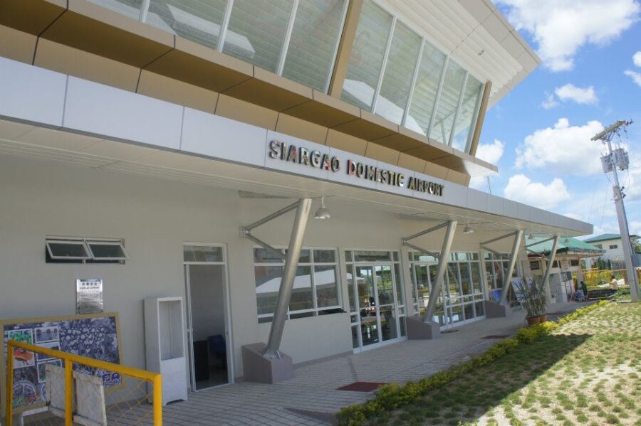 Siargao Sayak Airport domestic terminal exterior with modern glass facade and shaded promenade.