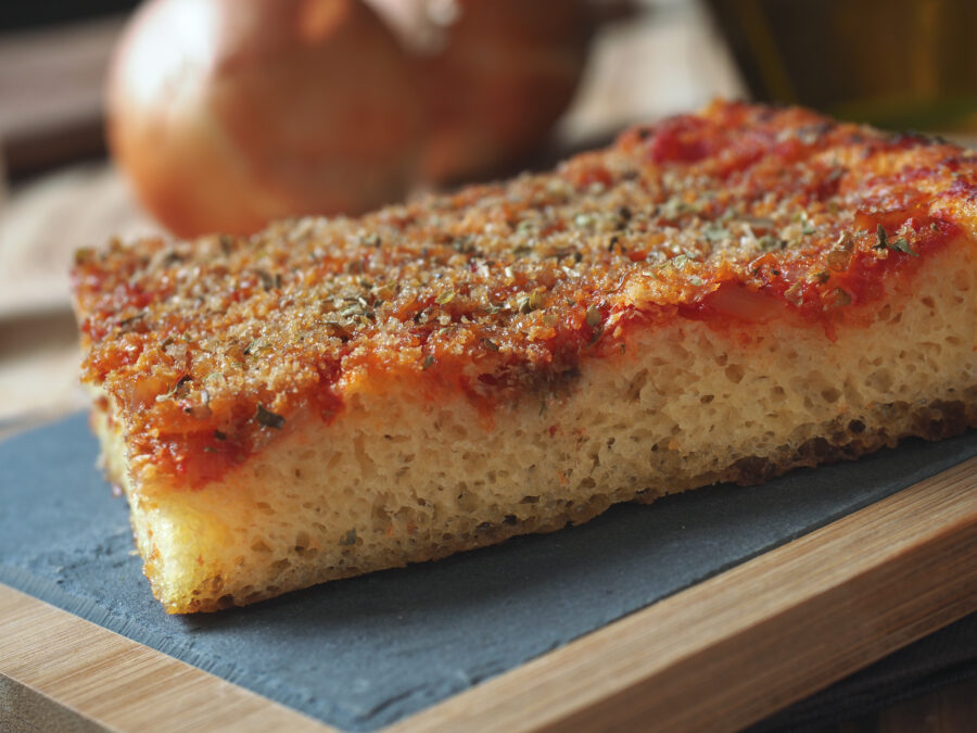 Traditional Sicilian sfincione, a thick, fluffy pizza topped with tomatoes, onions, and cheese, served on a wooden board
