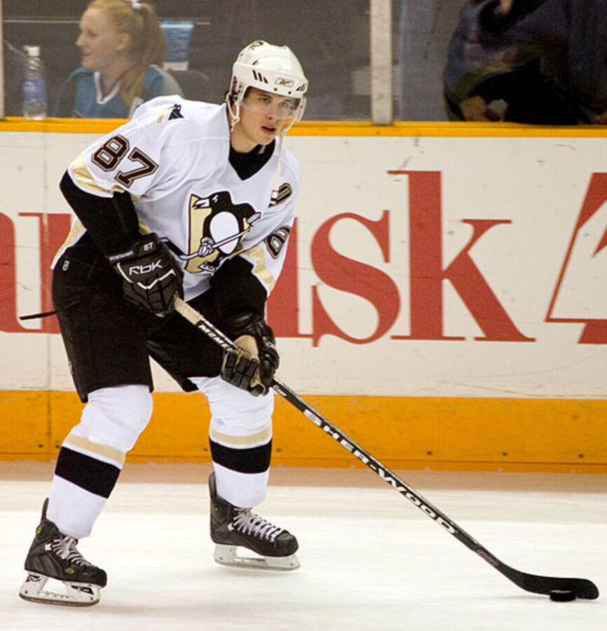 Sidney Crosby, professional ice hockey centre, wearing a team jersey and holding a hockey stick on the rink.
