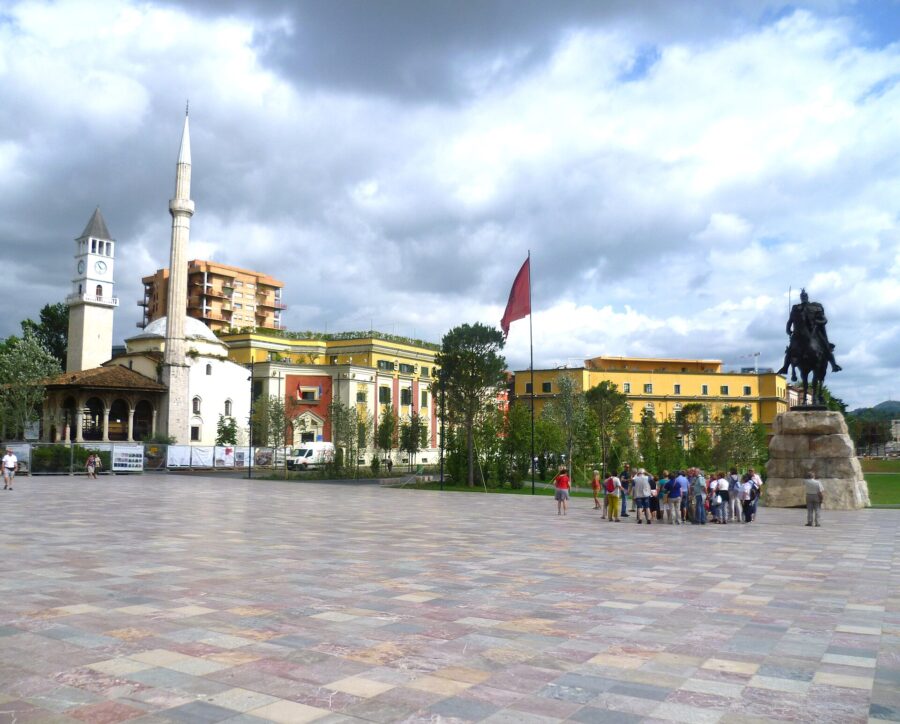 Skanderbeg Square in Tirana, Albania, bustling with people walking around a prominent statue in the center.