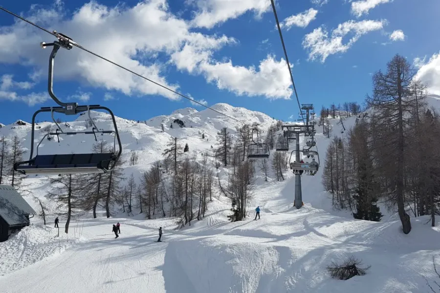 Vogel ski resort chairlift over sunny snowy alpine slopes with skiers.