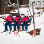 Ski resort with colorful ski suits, people on ski lift, snowy landscape, and vibrant activity.