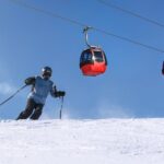 Skier in motion, blue sky, red gondolas, pristine snow, winter sports adventure.